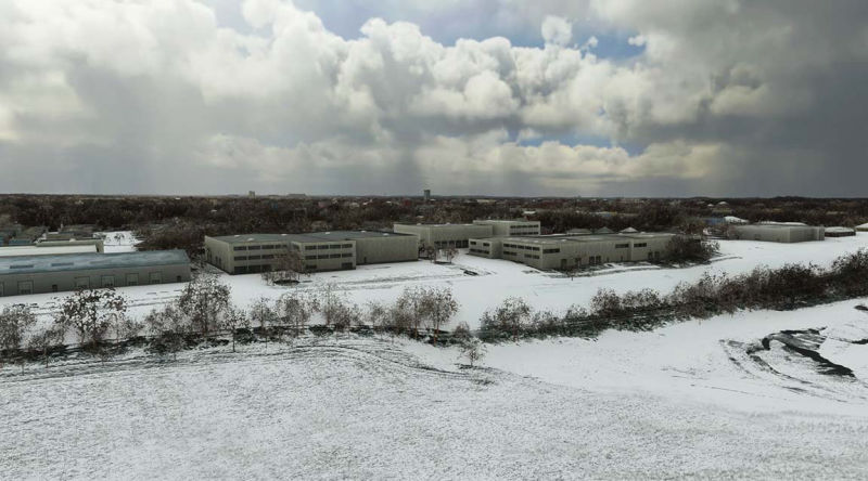 Aerial view of snowy field with leafless trees in winter landscape.