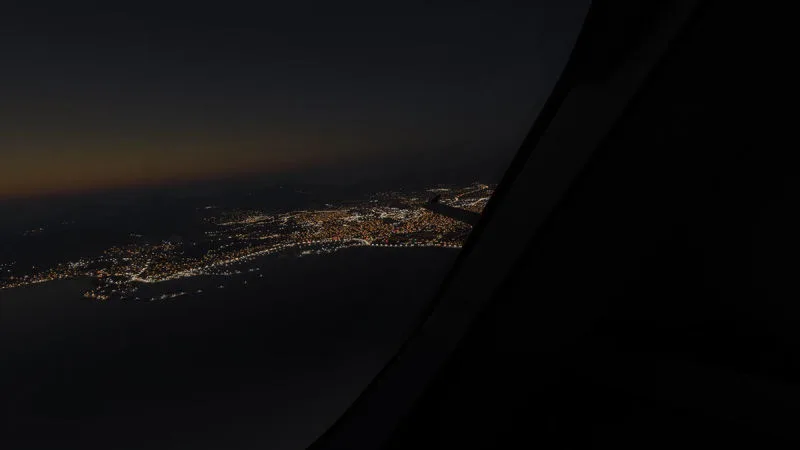 Coastal city lights at night seen from a dark cabin window, REX Atmos CORE night lighting in Microsoft Flight Simulator 2024