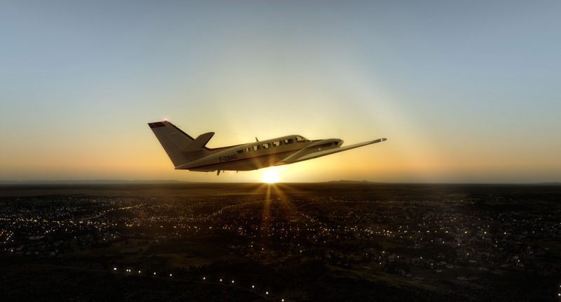 A small airplane flying over a city at sunset.