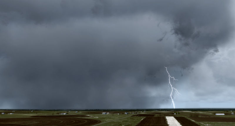 Storm clouds gathering over a field with a lightning bolt striking down.