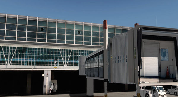 An airport terminal with a white, expansive building and a large truck nearby.